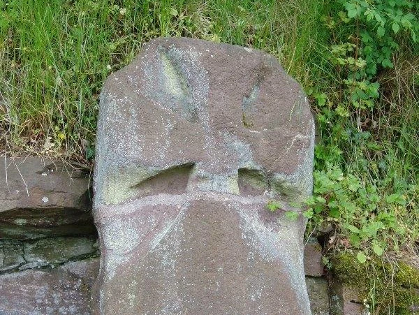 Der Kreuzstein Grauer Bundsandsteinblock mit einem steinernen Kreuz, umgeben von Gras