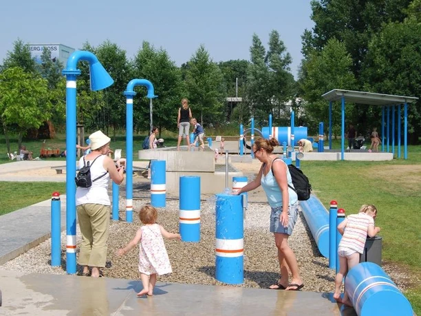 Ein Wasserspielplatz mit blauen Röhren, Kindern und Erwachsenen beim Spielen und Erkunden im Freien.