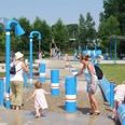 Wasserspielplatz Ein Wasserspielplatz mit blauen Röhren, Kindern und Erwachsenen beim Spielen und Erkunden im Freien.