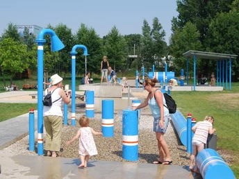 Wasserspielplatz Ein Wasserspielplatz mit blauen Röhren, Kindern und Erwachsenen beim Spielen und Erkunden im Freien.