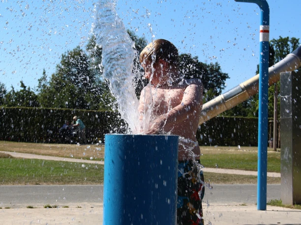 Ein Kind spielt im Sommer vergnügt an einem Wasserspielplatz mit sprudelndem Wasserstrahl.