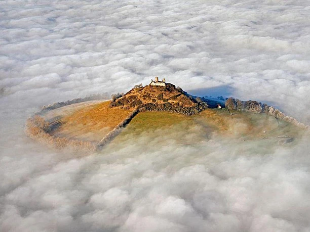Desenberg im Wolkenmeer Vulkanhügel Desenberg erhebt sich durch Nebel, mit zartem Sonnenlicht auf den Ruinen.