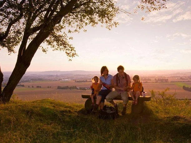 Picknick in der Abenddämmerung am Desenberg Eine Familie sitzt bei Sonnenuntergang auf einer Bank am Desenberg mit weitem Blick über Felder.