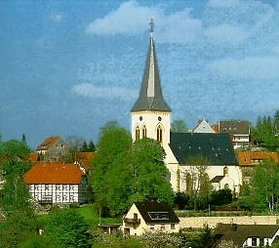 Die Alexanderkirche mit ihrem hohen Kirchturm umgeben von traditionellen Gebäuden und grünen Bäumen.
