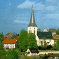 Die Alexanderkirche mit ihrem hohen Kirchturm umgeben von traditionellen Gebäuden und grünen Bäumen.