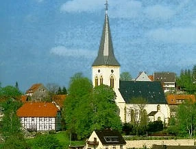 Die Alexanderkirche mit ihrem hohen Kirchturm umgeben von traditionellen Gebäuden und grünen Bäumen.