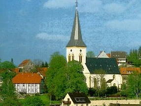 Alexanderkirche_Außenansicht Die Alexanderkirche mit ihrem hohen Kirchturm umgeben von traditionellen Gebäuden und grünen Bäumen.
