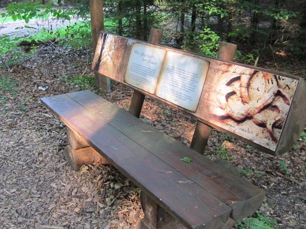 Holzbank auf dem Mythenweg Herlingsburg in einem Wald, mit einer Infotafel zu lokalen Sagen.