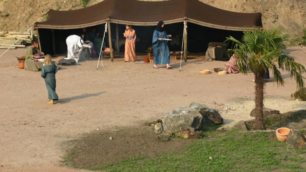 Bibeldorf Rietberg Menschen in traditioneller Kleidung vor einem Beduinenzelt in einer Wüstenkulisse mit Palmen.