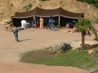Bibeldorf Rietberg Menschen in traditioneller Kleidung vor einem Beduinenzelt in einer Wüstenkulisse mit Palmen.