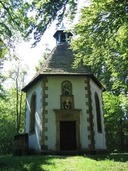 Vituskapelle Willebadessen Achteckige Kapelle im Wald mit Schieferdach und Turm, umgeben von grüner Natur, unten Zugangstür.