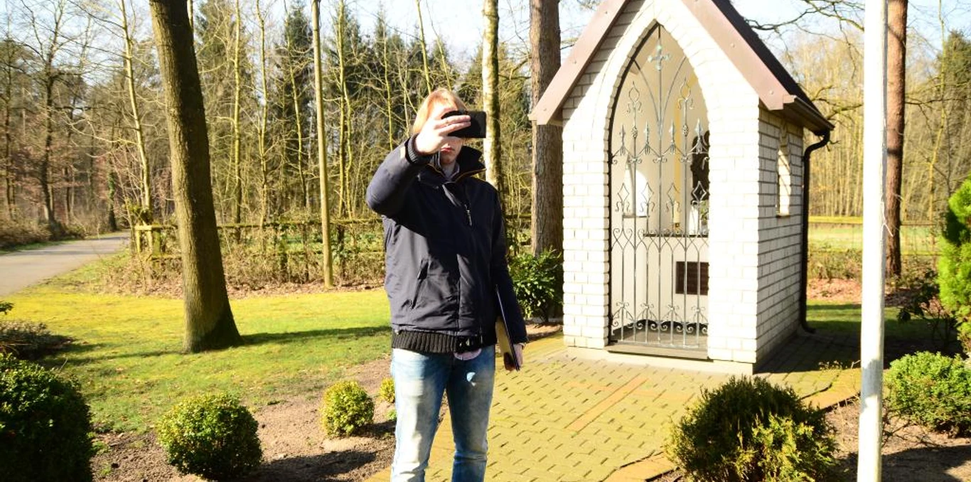 Heiligenhäuschen am Wapelweg Ein Mann macht ein Selfie vor einem kleinen, weißen Heiligenhäuschen im sonnigen Wald.