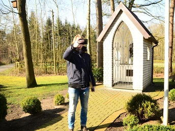 Heiligenhäuschen am Wapelweg Ein Mann macht ein Selfie vor einem kleinen, weißen Heiligenhäuschen im sonnigen Wald.