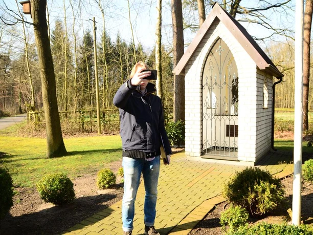 Heiligenhäuschen am Wapelweg Ein Mann macht ein Selfie vor einem kleinen, weißen Heiligenhäuschen im sonnigen Wald.