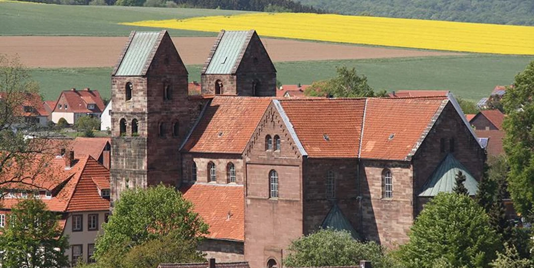 Fredelsloh Zwei markante Kirchtürme von Fredelsloh ragen über rote Dächer hinaus, umgeben von grünen Feldern.