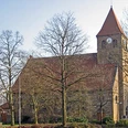 Steinernen Kirche Kirchlengern mit rotem Dach, Glockenturm und kahlen Bäumen im Vordergrund.