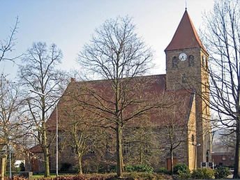 Steinernen Kirche Kirchlengern mit rotem Dach, Glockenturm und kahlen Bäumen im Vordergrund.