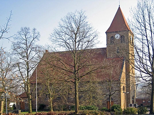 Kirche Kirchlengern Steinernen Kirche Kirchlengern mit rotem Dach, Glockenturm und kahlen Bäumen im Vordergrund.
