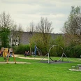 Mehrgenerationenpark Spielplatz mit Schaukeln und Rutschen im Mehrgenerationenpark, umgeben von grüner Wiese und Bäumen.