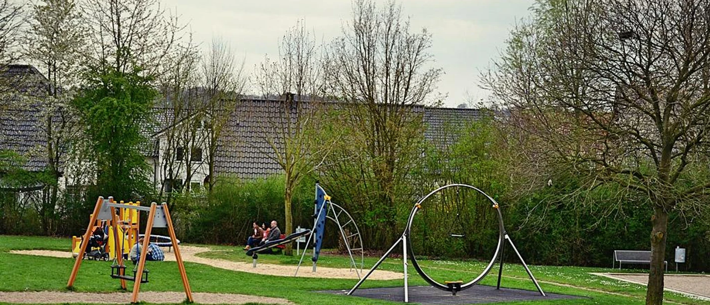 Mehrgenerationenpark Spielplatz mit Schaukeln und Rutschen im Mehrgenerationenpark, umgeben von grüner Wiese und Bäumen.