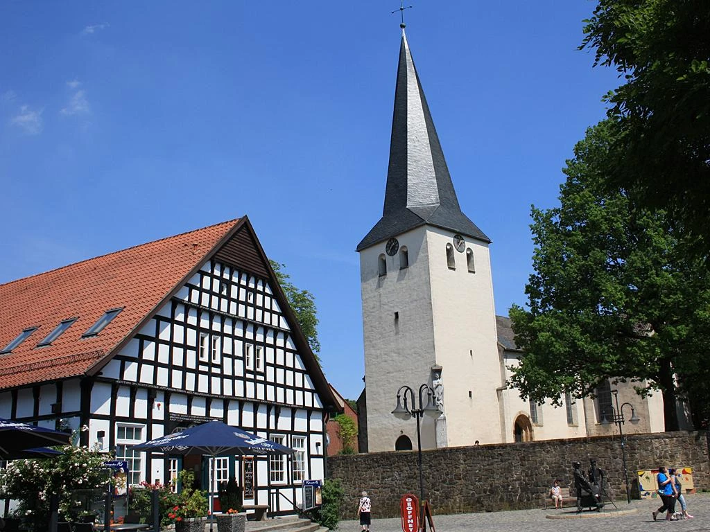 Historische Laurentiuskirche mit markantem spitzen Turm neben einem Fachwerkhaus, blauer Himmel.