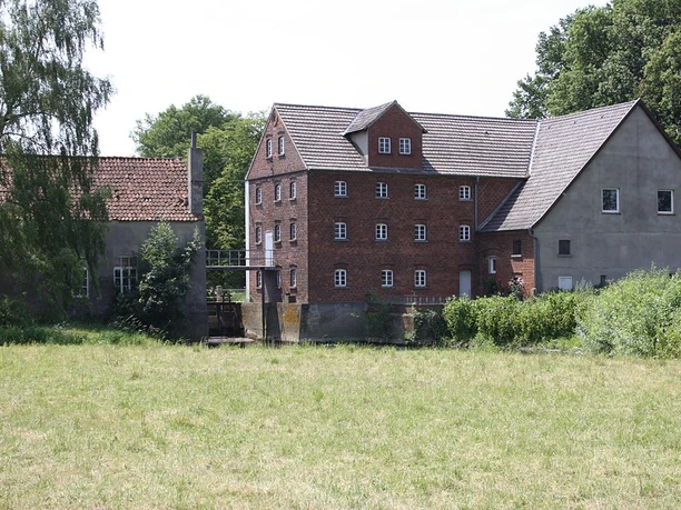 Historische Backsteinmühle in Nienburg an der Else, umgeben von saftigem Grün und alten Bäumen.