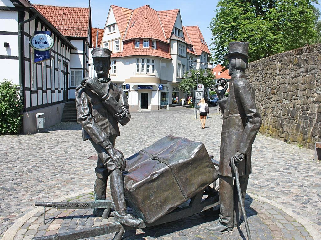 Steinmeister- und Wellensiek-Denkmal Bronzeskulptur von zwei Männern mit Pferdekarren auf Kopfsteinpflasterstraße im urbanen Umfeld.