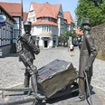 Steinmeister- und Wellensiek-Denkmal Bronzeskulptur von zwei Männern mit Pferdekarren auf Kopfsteinpflasterstraße im urbanen Umfeld.