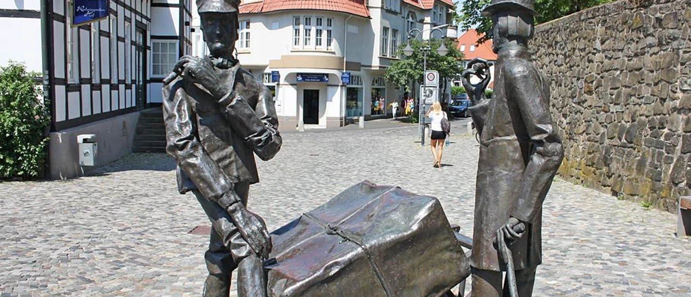 Steinmeister- und Wellensiek-Denkmal Bronzeskulptur von zwei Männern mit Pferdekarren auf Kopfsteinpflasterstraße im urbanen Umfeld.