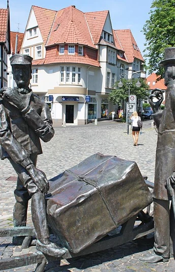 Steinmeister- und Wellensiek-Denkmal Bronzeskulptur von zwei Männern mit Pferdekarren auf Kopfsteinpflasterstraße im urbanen Umfeld.