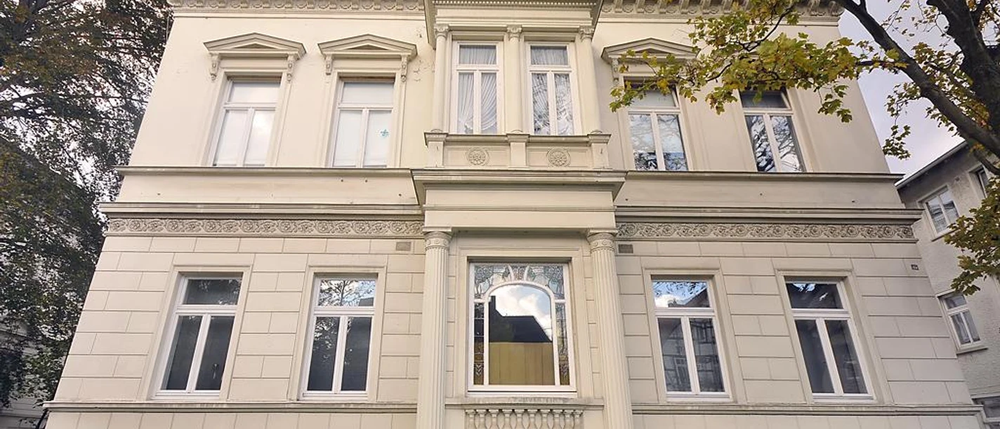 Eine weiße, historische Villa mit symmetrischen Fenstern und dekorativen Fassadenelementen.
