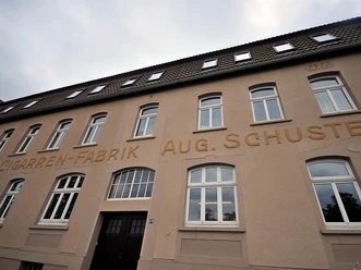 Zigarrenfabrik „August Schuster“ Historische Zigarrenfabrik August Schuster mit klassischer Backsteinfassade und großen Fenstern.