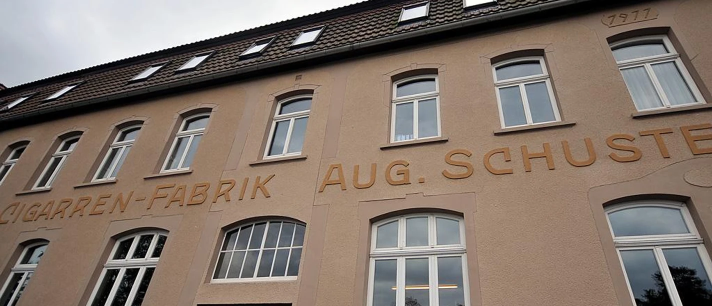Zigarrenfabrik „August Schuster“ Historische Zigarrenfabrik August Schuster mit klassischer Backsteinfassade und großen Fenstern.