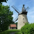 Liesbergmühle Historische Liesbergmühle mit markanten Flügeln, umgeben von üppigem Grün und einem Nebengebäude.