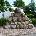 Elsternbuschdenkmal Steinhaufen-Denkmal aus glatten, großen Felsen, umgeben von grünen Hecken und Bäumen.