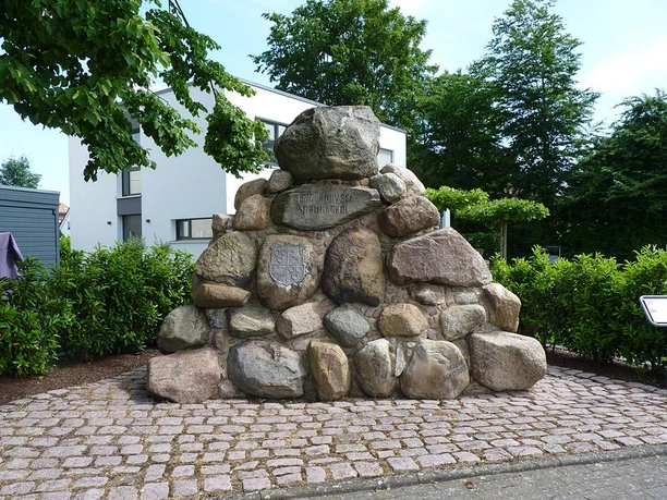 Elsternbuschdenkmal Steinhaufen-Denkmal aus glatten, großen Felsen, umgeben von grünen Hecken und Bäumen.