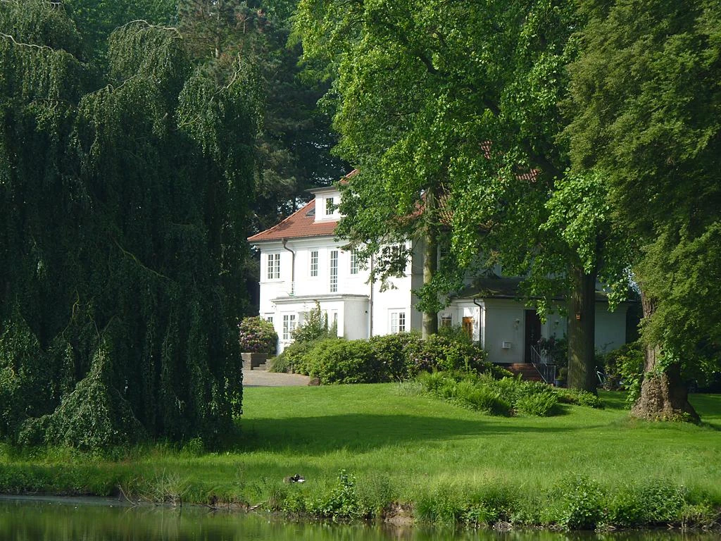 Ein weitläufiges Anwesen mit einem weißen Herrenhaus, umgeben von üppigem Grün und hohen Bäumen.