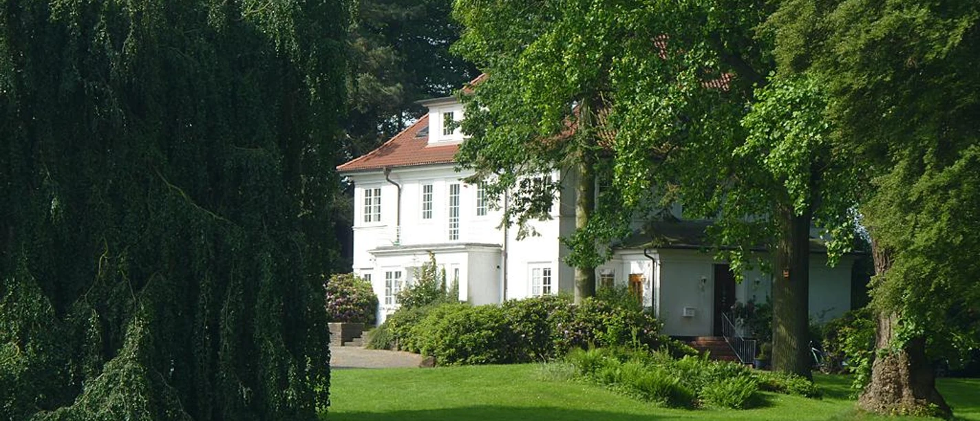 Sattelmeier Baringhof Ein weitläufiges Anwesen mit einem weißen Herrenhaus, umgeben von üppigem Grün und hohen Bäumen.