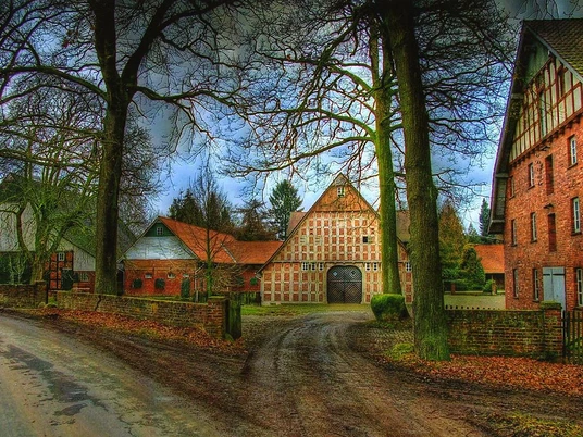 Historischer Hof mit Fachwerkgebäuden, von Bäumen umgeben, auf einem ländlichen Grundstück.