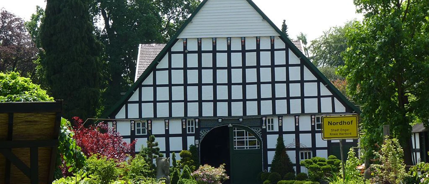Fachwerkhaus mit markantem Spitzdach, umgeben von üppigem Grün und gepflegten Gartenanlagen.