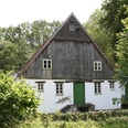 Steinbecker Mühle Alte Wassermühle in ländlicher Umgebung, halb Fachwerk, halb gemauert, flankiert von Bäumen.