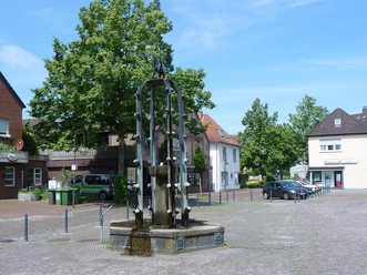 Der Widukindbrunnen steht auf einem gepflasterten Platz, umgeben von Bäumen und historischen Gebäuden.