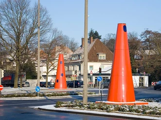 Safety Cones Große rote Kegel auf einem schneebedeckten Kreisverkehr in urbaner Umgebung mit Häusern im Hintergrund.