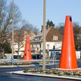 Safety Cones Große rote Kegel auf einem schneebedeckten Kreisverkehr in urbaner Umgebung mit Häusern im Hintergrund.