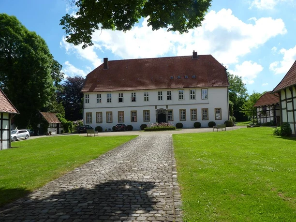 Historisches zweistöckiges Gebäude mit Satteldach, umgeben von gepflegtem Rasen und gepflastertem Weg.