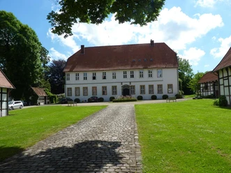 Gut Hiddenhausen Historisches zweistöckiges Gebäude mit Satteldach, umgeben von gepflegtem Rasen und gepflastertem Weg.