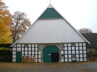 Historischer Fachwerkbau mit grünem Tor und herbstlichem Laub, umrahmt von großen Bäumen.