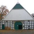 Historischer Fachwerkbau mit grünem Tor und herbstlichem Laub, umrahmt von großen Bäumen.
