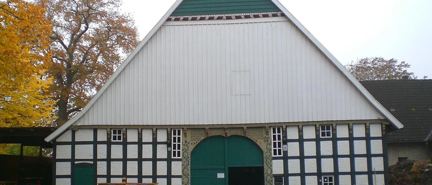 Historischer Fachwerkbau mit grünem Tor und herbstlichem Laub, umrahmt von großen Bäumen.