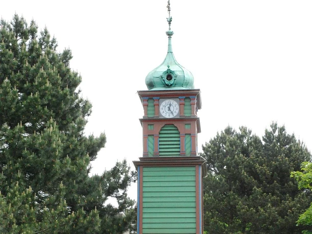 MeyLip-Turm Grün verkleideter Turm mit Kupferkuppel, Ziffernblatt und umrahmt von dichten Kiefern.